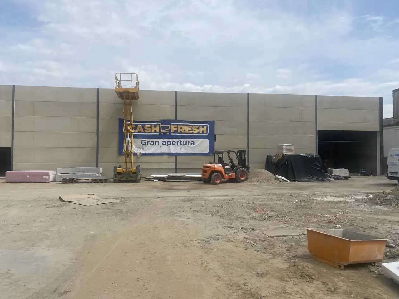Fachada con el cartel de gran apertura y maquinaria en obra