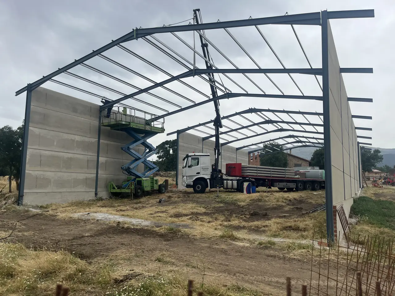 Montaje con el camión grúa de Estrucserena cargado de placas y plataforma elevadora entre los pórticos