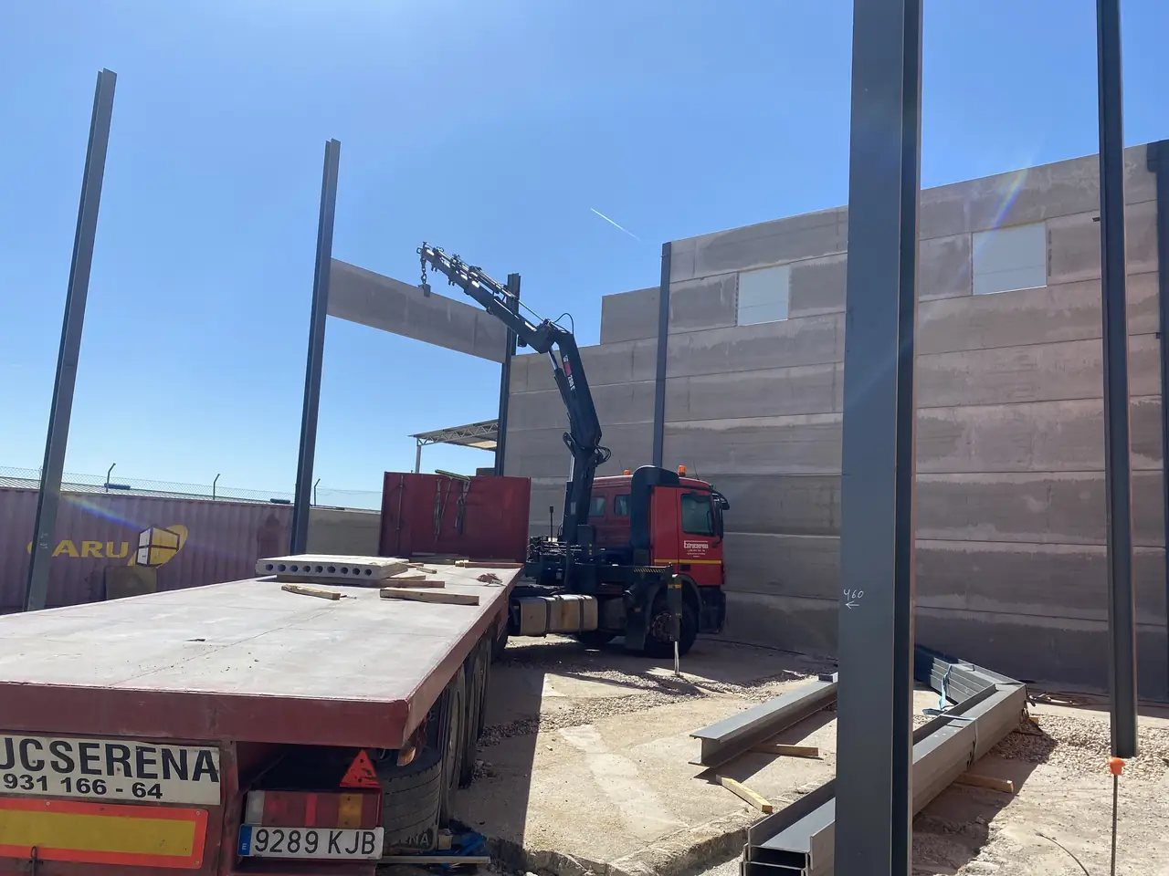 Camión grúa con placas cargadas colocando una placa junto a la nave