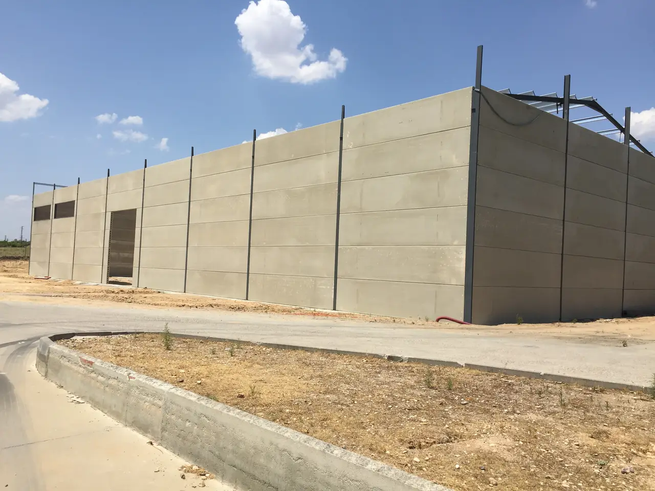 Nave con el cerramiento de placas montado, huecos de ventana y de acceso y la estructura metálica en la parte superior